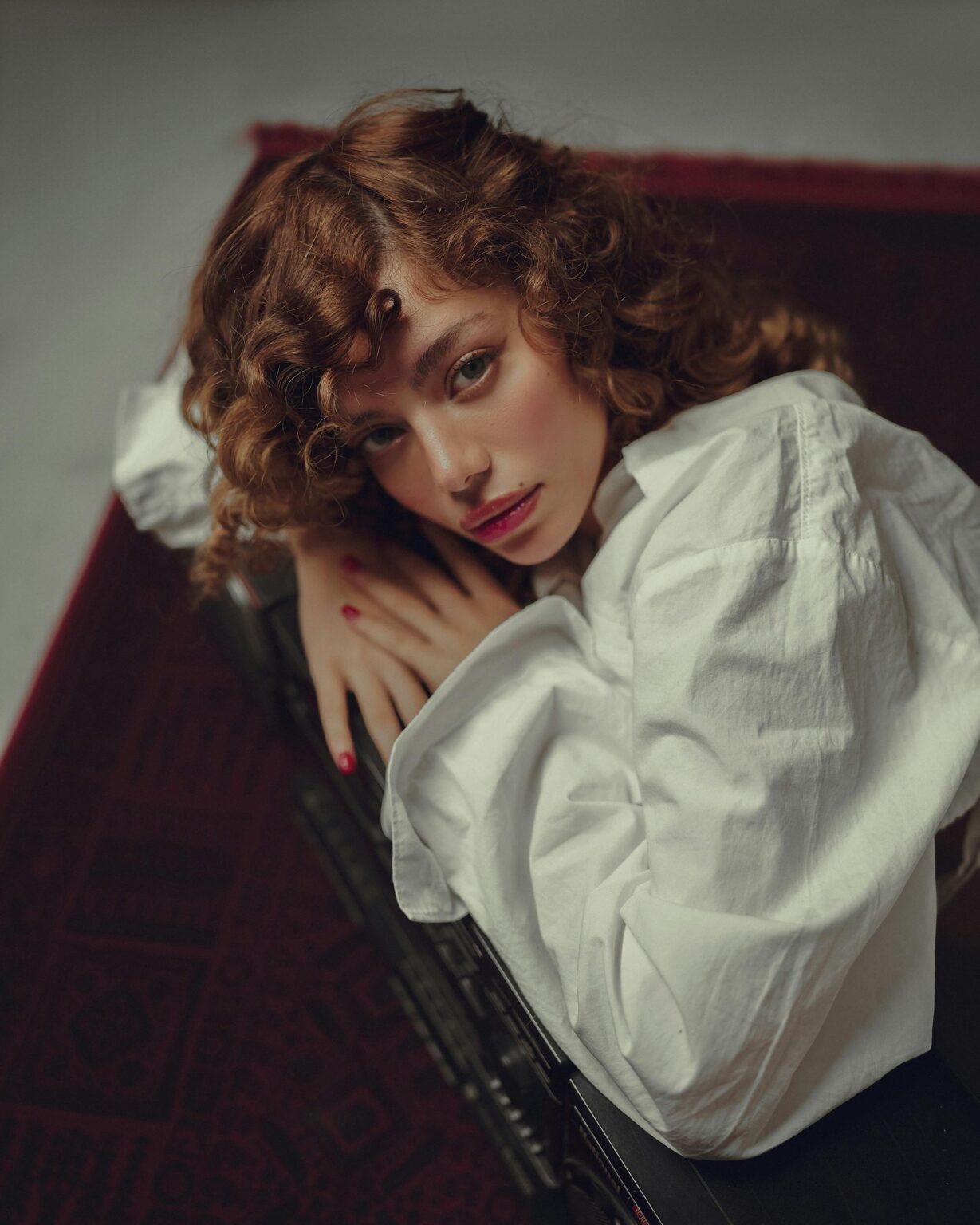 Artistic portrait of a woman lying on a carpet with a curly hairstyle and white shirt.